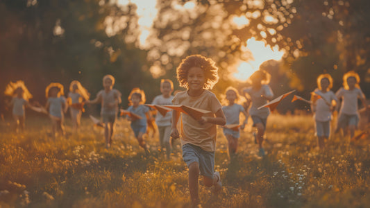 Children running through a soft sunlit field with paper airplanes, symbolizing confidence, play, emotional safety and the gentle psychologist-designed parenting guide on affirmations for kids by Talk2Tessa.