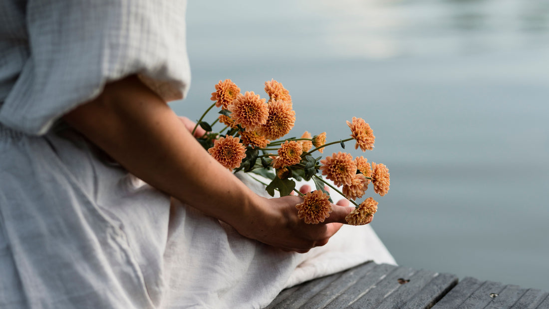 Woman by the water with blooming flowers, symbolising emotional healing and the stages of burnout recovery, illustrated in this Talk2Tessa psychologist guide.