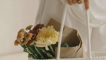 Woman holding a grocery bag with flowers, symbolizing a gentle and compassionate relationship with money, used as the hero image for a psychologist-written article on money affirmations.