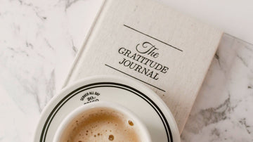 Gratitude journal on a marble table beside a cup of coffee — a calm, psychologist-written self-help moment with Talk2Tessa.