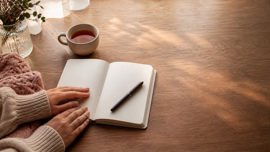 Open journal, gold pen, tea, and dusty-rose knit in soft window light on a warm wooden table.