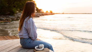 Woman sitting peacefully by the water, reflecting and journaling as a symbol of emotional healing, self-compassion, and gentle self-discovery.