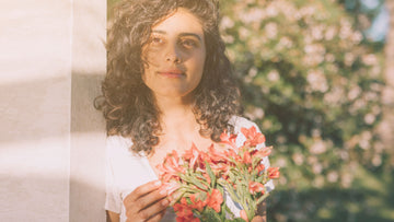 Joyful woman surrounded by soft flowers, symbolizing gentle growth and soft success — Talk2Tessa psychologist-guided self-help.