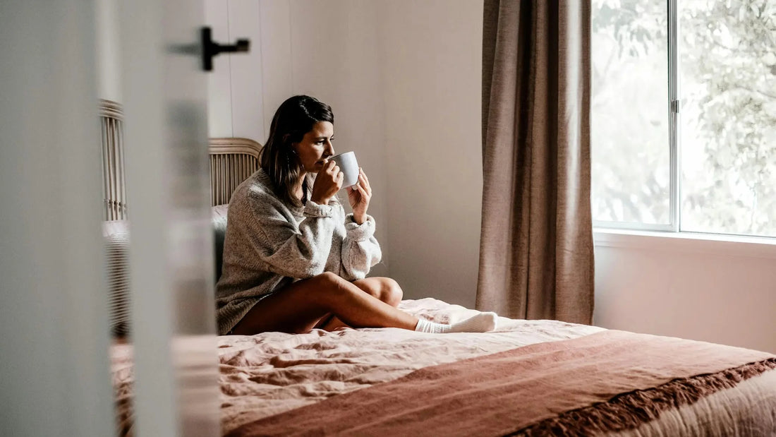 Woman sitting on a bed feeling emotionally overwhelmed and lost in thought, representing self-doubt and overthinking.