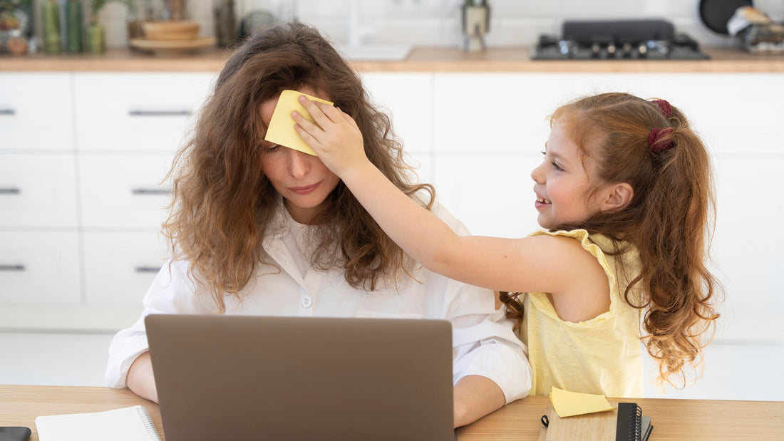 A mom trying to work on her laptop while her child places a post-it on her head, symbolizing mom burnout, overwhelm, and gentle ACT and self-compassion recovery with Talk2Tessa.